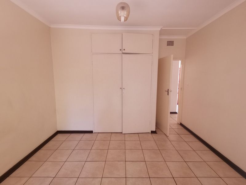 An empty bedroom featuring tiled flooring and built-in cupboards with overhead storage compartments.