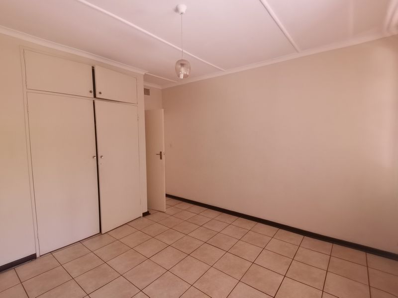 A clean, empty bedroom featuring neutral tiled flooring, built-in cupboards, and a simple ceiling light fixture, offering a blank canvas for personalization.
