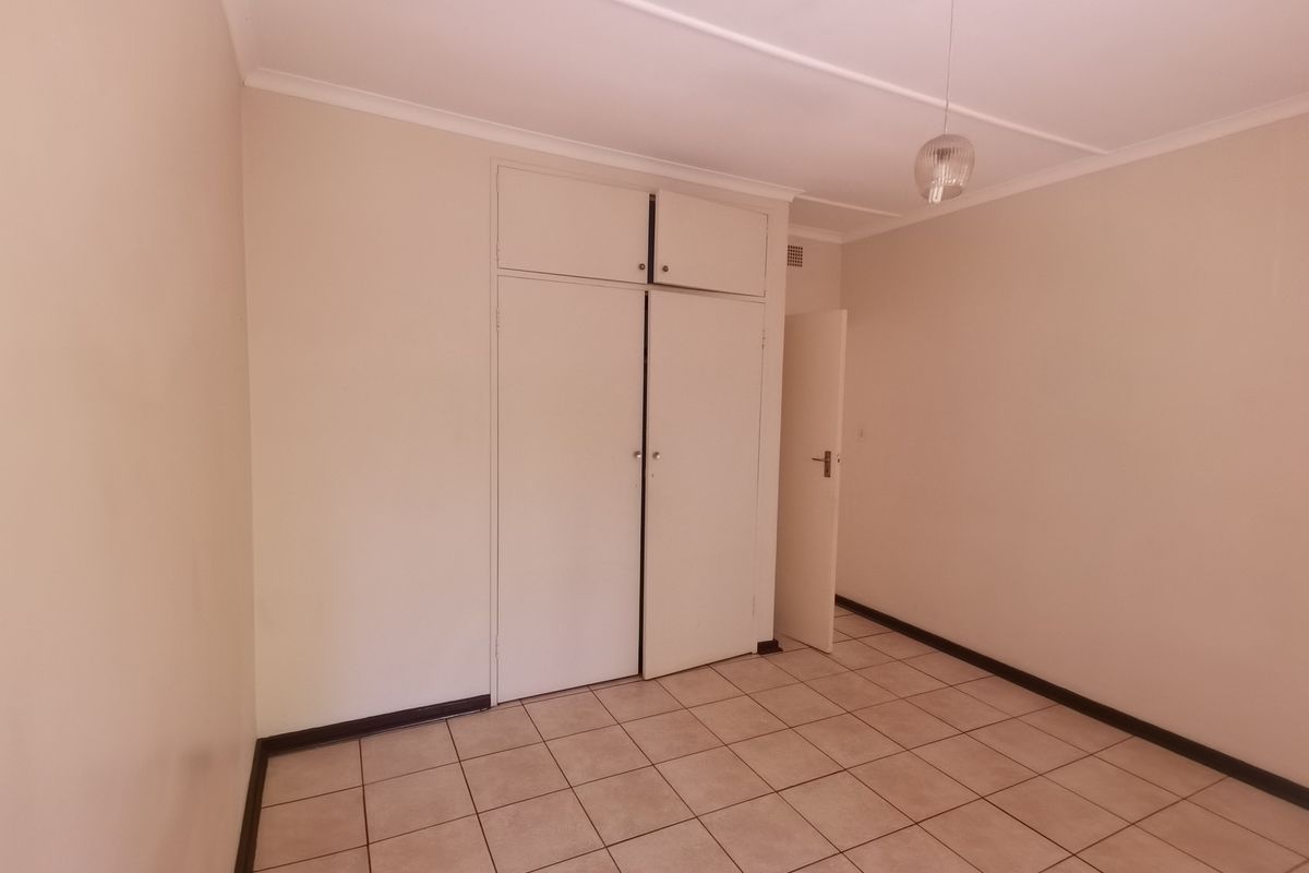 A clean, empty bedroom featuring neutral tiled flooring and built-in cupboards, offering a blank canvas for personalization.