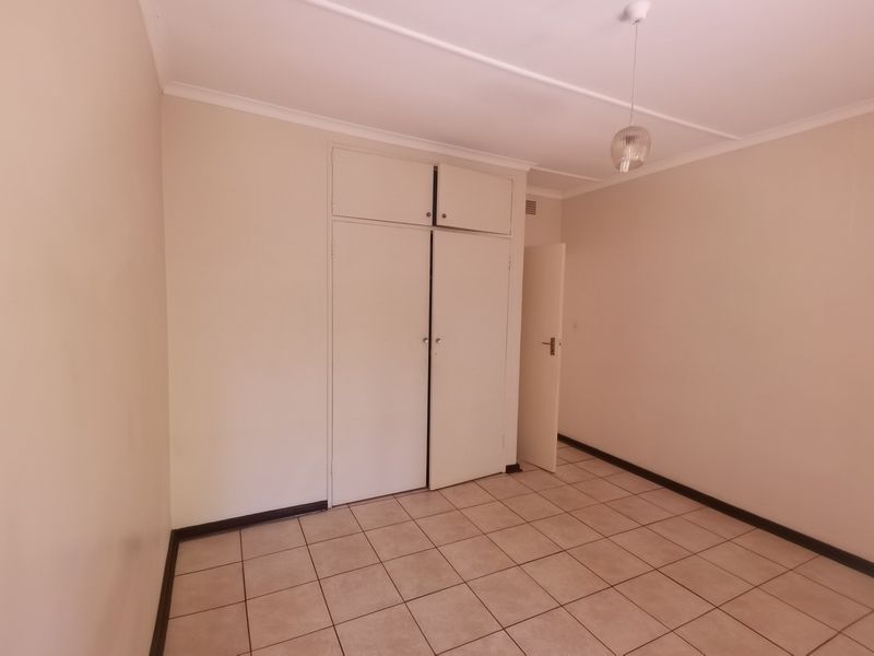 A clean, empty bedroom featuring neutral tiled flooring and built-in cupboards, offering a blank canvas for personalization.