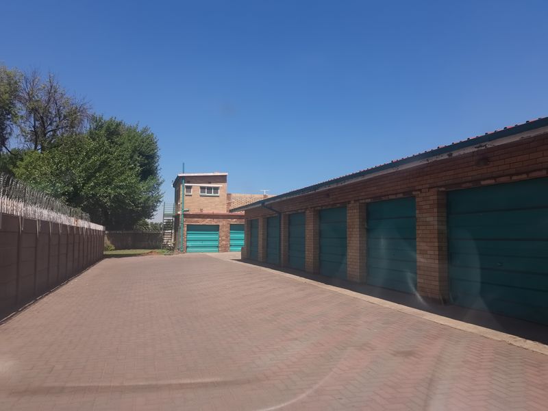 A row of garages with brick construction and paved driveway access, secured by a perimeter wall with razor wire.