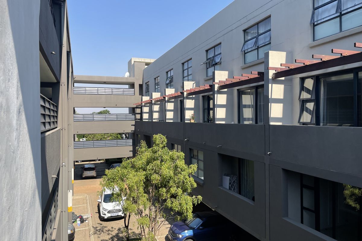 Exterior view of a modern apartment complex featuring multi-level balconies with pergolas, paved parking areas, and well-maintained building facades.