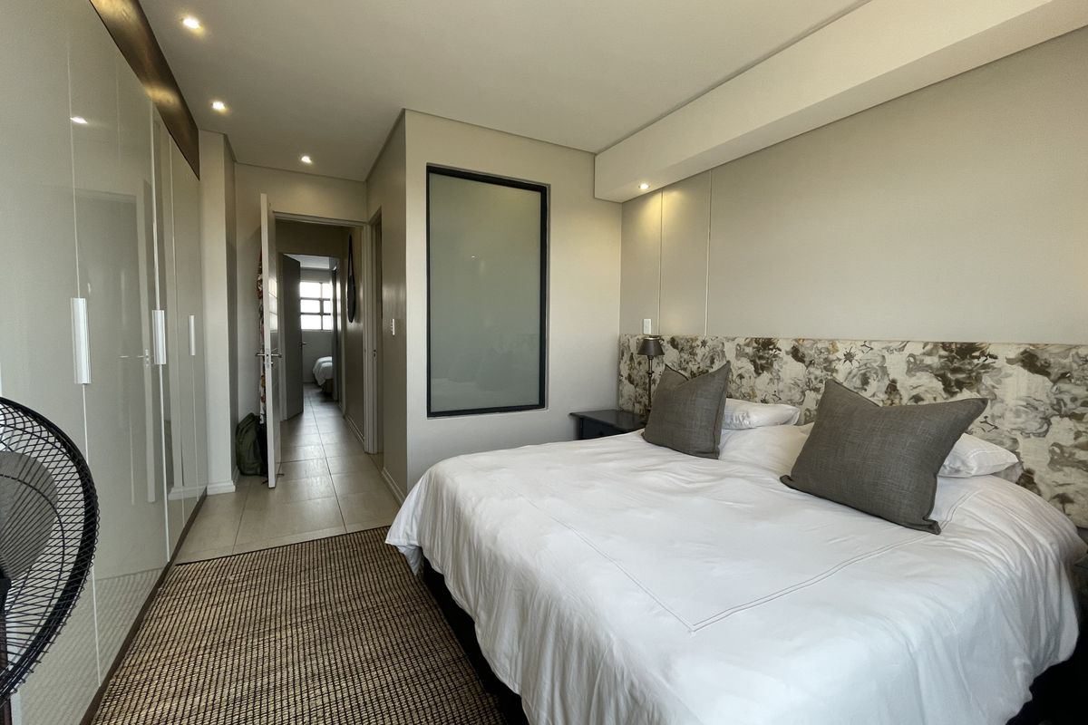 Modern bedroom featuring high-gloss built-in cupboards, recessed lighting, and a unique frosted glass feature panel, leading into a tiled hallway.