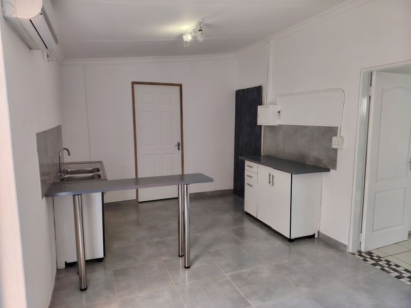 A functional, empty kitchen area featuring white cabinetry, grey laminate countertops, a double sink, and tiled flooring, with an installed air conditioning unit.
