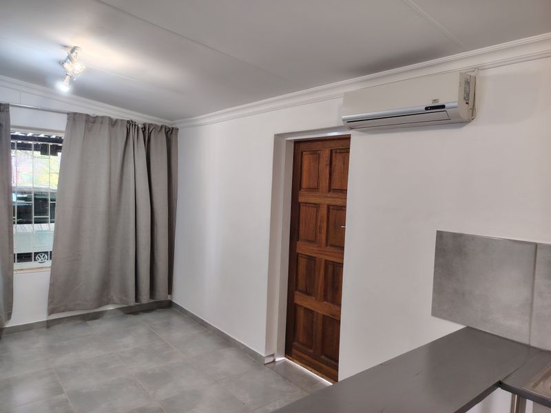 An open-plan living area featuring tiled flooring, a split-system air conditioner, and a solid timber door, presenting a clean and neutral space.