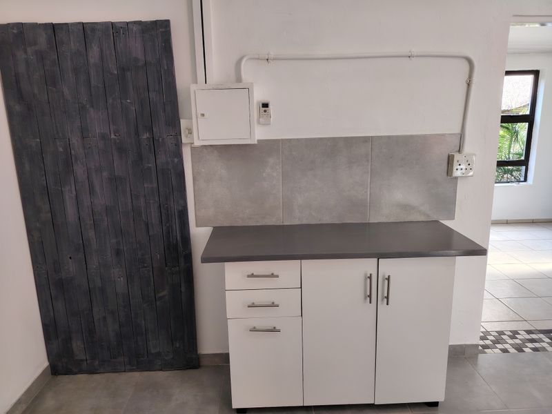 A functional scullery or utility area featuring built-in white cabinetry, a dark laminate countertop, and a modern grey tiled splashback.