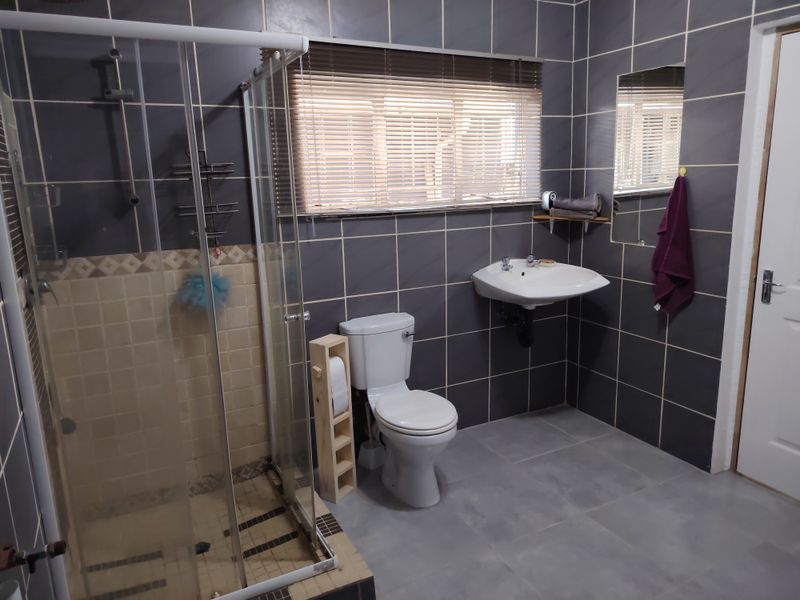 A functional bathroom featuring a glass shower enclosure, wall-mounted basin, toilet, and dark grey wall tiling with a contrasting tiled floor.