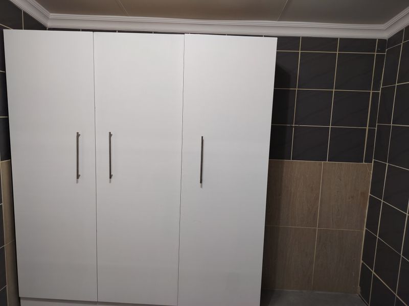 A bedroom featuring a modern white built-in wardrobe set against a two-tone tiled wall with crown molding.