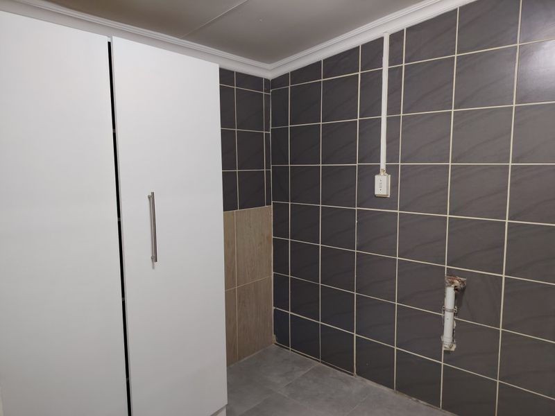 A functional laundry area featuring tiled walls, built-in cabinetry, and dedicated plumbing connections for appliances.