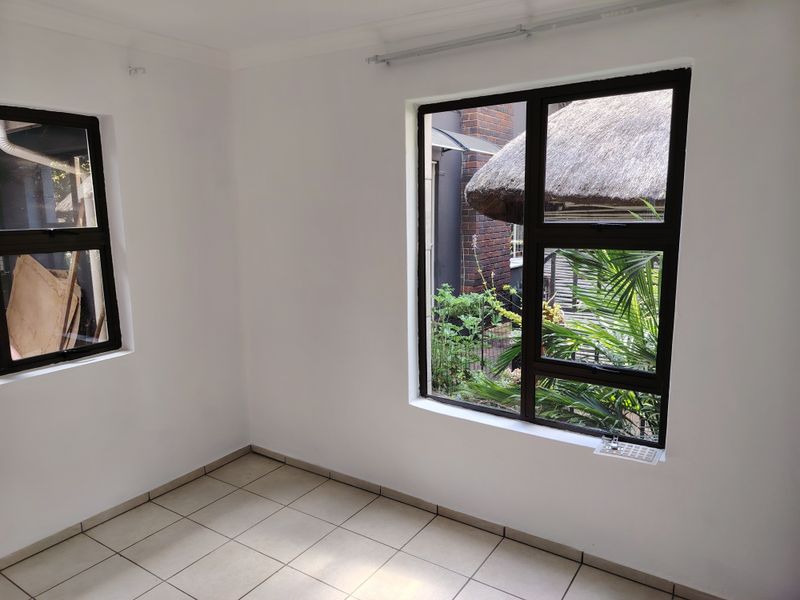 A bright, empty bedroom featuring neutral tiled flooring and dark aluminium window frames with views of the garden.