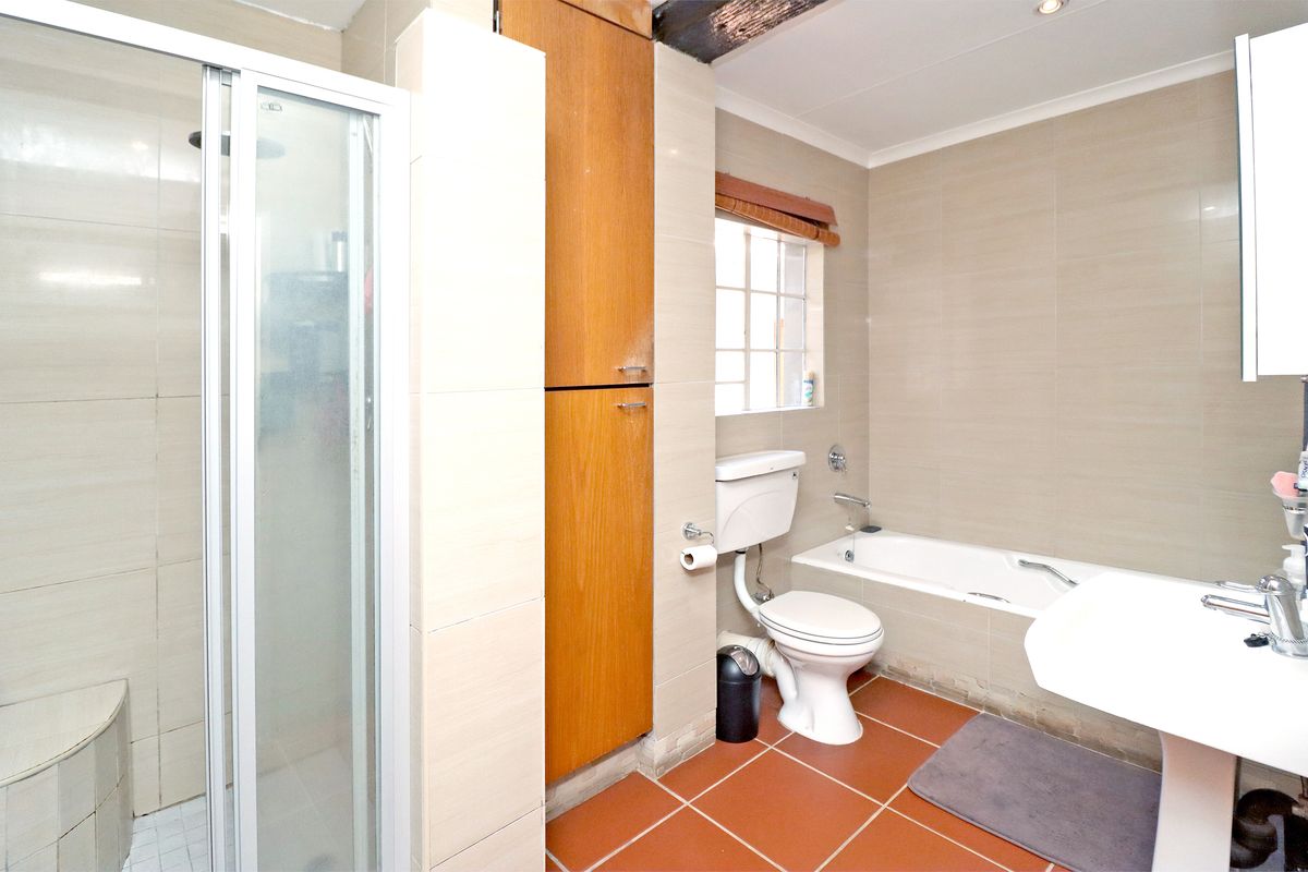 A functional bathroom featuring a shower enclosure, bathtub, pedestal basin, and built-in storage cabinetry with neutral wall tiling and terracotta floor tiles.