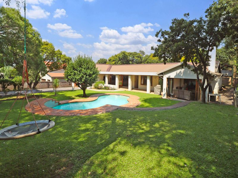 Spacious rear garden featuring a swimming pool with brick coping, a covered patio area, and established trees, providing a private outdoor living space.