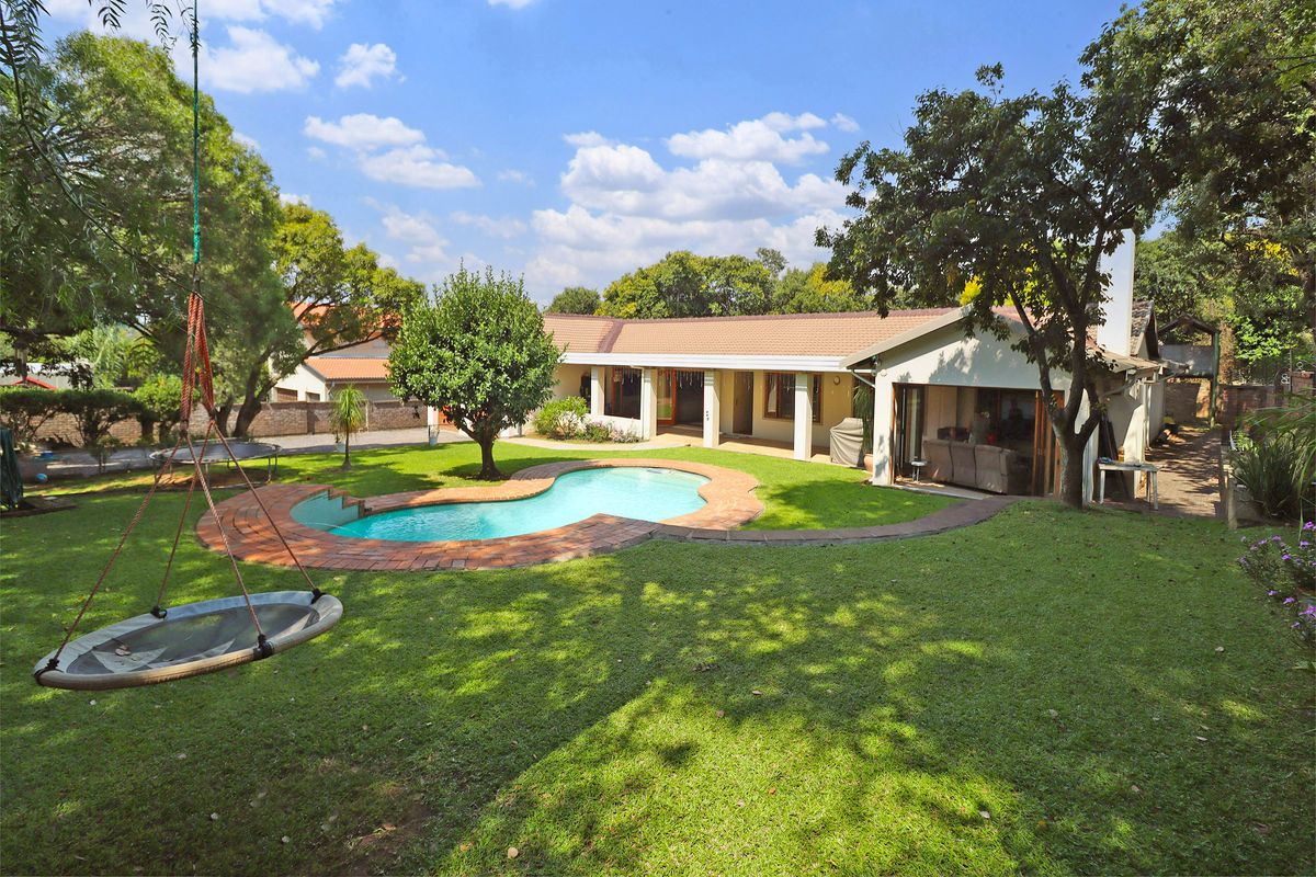 Spacious rear garden featuring a swimming pool with brick coping, a covered patio area, and established trees, providing a private outdoor living space.