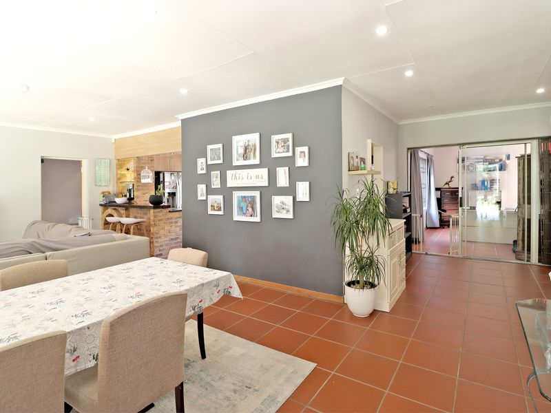 Spacious open-plan living and dining area featuring terracotta floor tiles, recessed lighting, and a brick breakfast bar connecting to the kitchen.