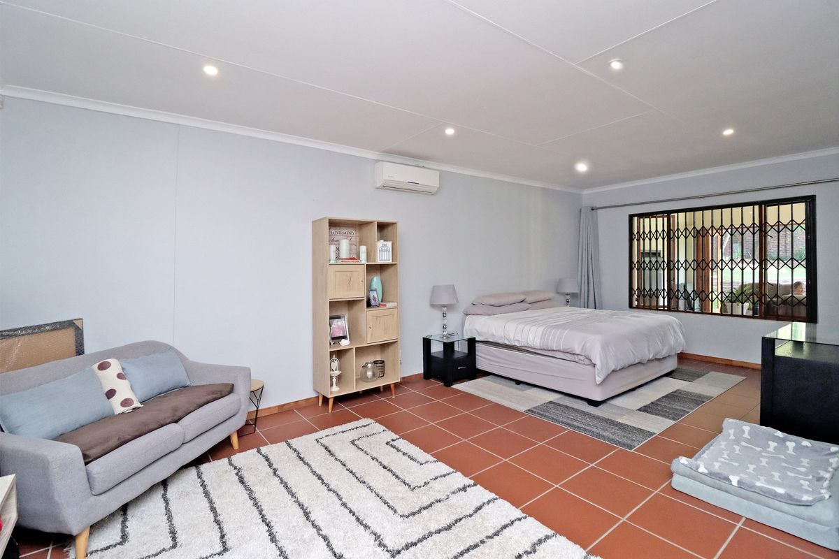 Spacious bedroom featuring tiled flooring, recessed downlighting, and a wall-mounted air conditioning unit, with security bars installed on the window.