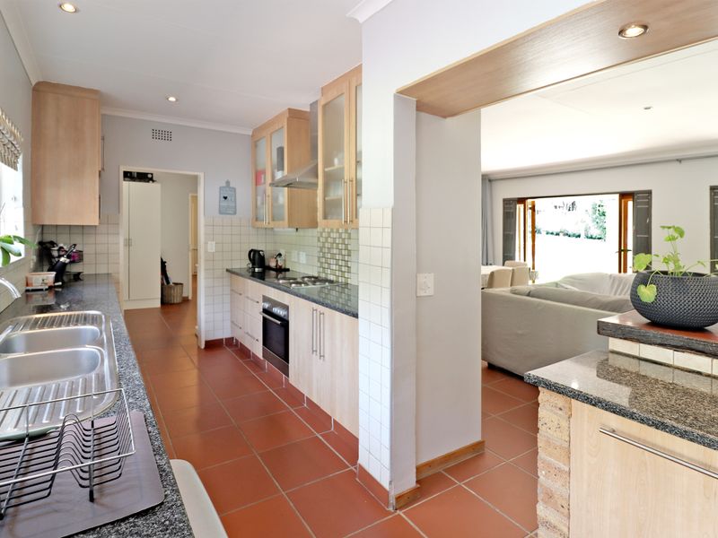 Functional kitchen featuring light wood cabinetry, granite countertops, tiled flooring, and integrated appliances, with an open-plan flow into the adjacent living area.
