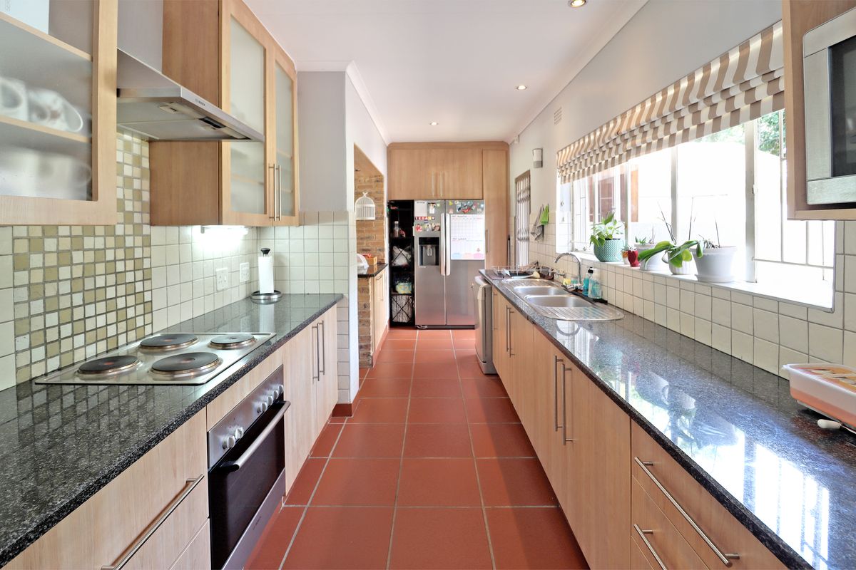 A functional galley-style kitchen featuring granite countertops, light wood cabinetry, tiled splashbacks, and integrated appliances, offering a clean and practical workspace.