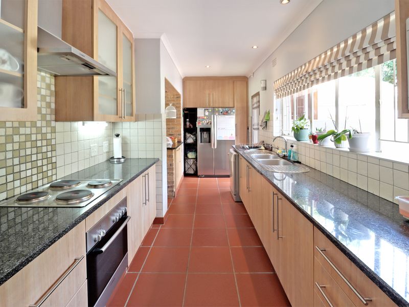 A functional galley-style kitchen featuring granite countertops, light wood cabinetry, tiled splashbacks, and integrated appliances, offering a clean and practical workspace.