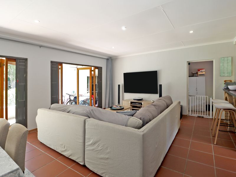 Open-plan living area featuring terracotta floor tiles, recessed lighting, and an exposed brick breakfast bar, with direct access to an outdoor patio.