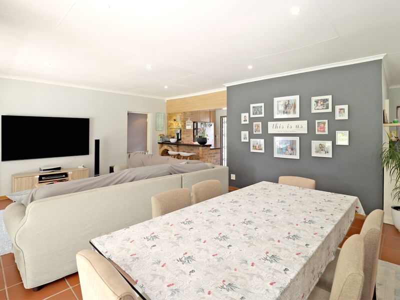 Spacious open-plan living and dining area featuring terracotta floor tiles, recessed lighting, and a brick breakfast bar connecting to the kitchen.