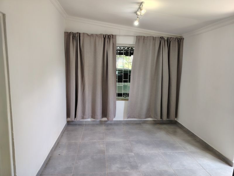 A clean, empty bedroom featuring neutral tiled flooring, security bars on the window, and a modern ceiling-mounted spotlight fixture.