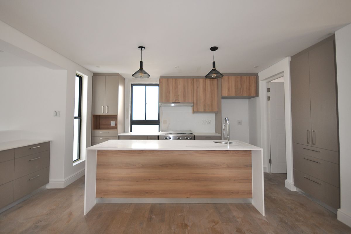 Modern kitchen featuring a central island with a sink, wood-grain cabinetry, stone countertops, and integrated stainless steel appliances.