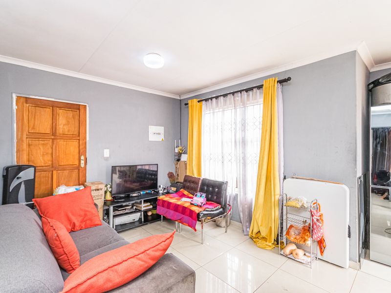 A functional living room featuring tiled flooring, a security gate on the window, and neutral wall finishes, offering a practical space for daily living.