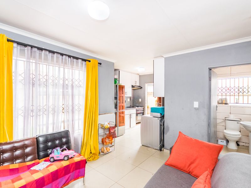 Open-plan living area featuring tiled floors, a functional kitchen with built-in cabinetry, and an adjacent bathroom with standard fixtures.