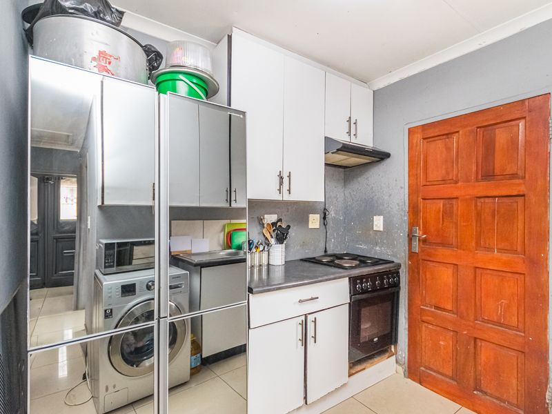 Compact kitchen featuring white cabinetry, built-in oven and stove, extractor fan, and tiled flooring, with direct access to an adjacent room.