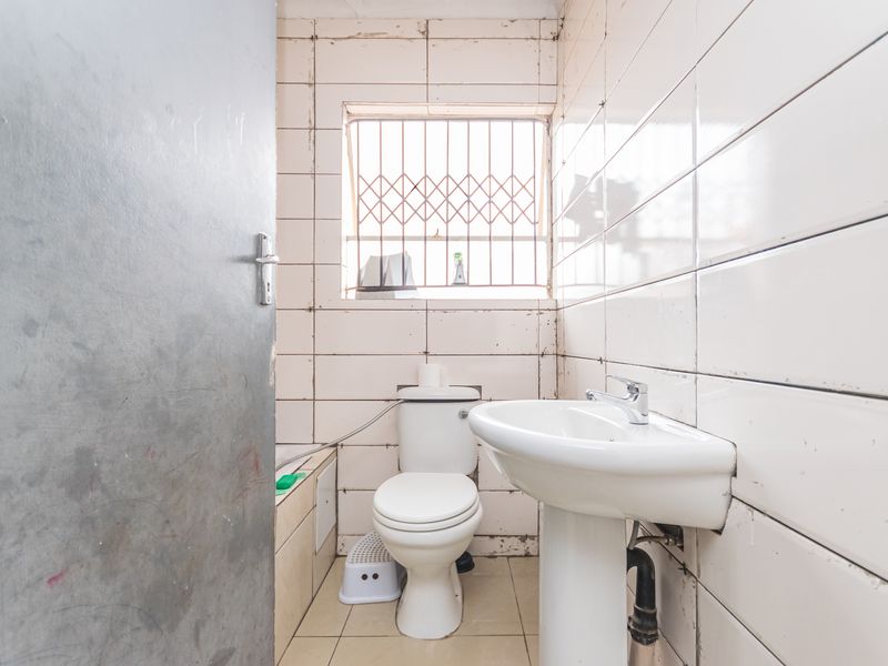 A compact bathroom featuring a pedestal basin and toilet with tiled walls, requiring cosmetic updates and repairs to finishes.
