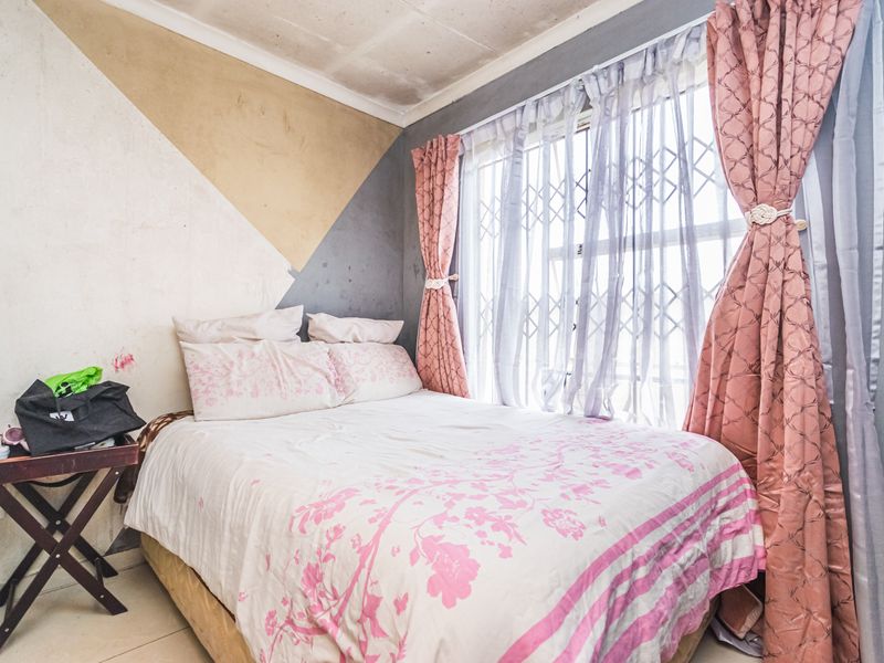 A bedroom featuring tiled flooring, a security gate on the window, and decorative wall paint, currently requiring maintenance and cosmetic updates.