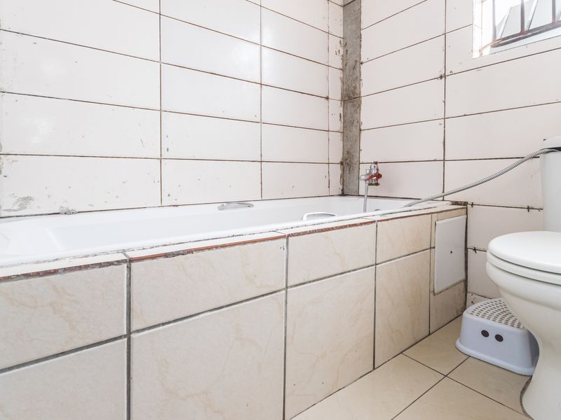 A functional bathroom featuring a bathtub and toilet with tiled walls and flooring, currently requiring maintenance and cosmetic updates to improve its overall condition.