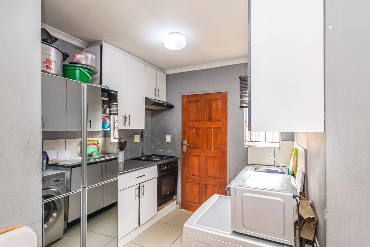 A functional kitchen featuring built-in cabinetry, a stove with extractor fan, and tiled flooring, providing a practical workspace with direct access to an exterior door.