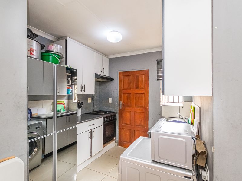 A functional kitchen featuring built-in cabinetry, a stove with extractor fan, and tiled flooring, providing a practical workspace with direct access to an exterior door.