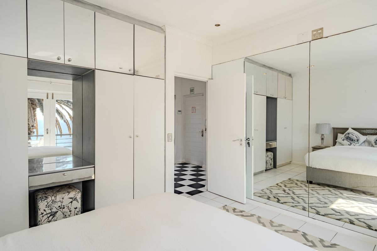 A bright bedroom featuring extensive built-in cabinetry with mirrored wardrobe doors, tiled flooring, and a dedicated vanity area.