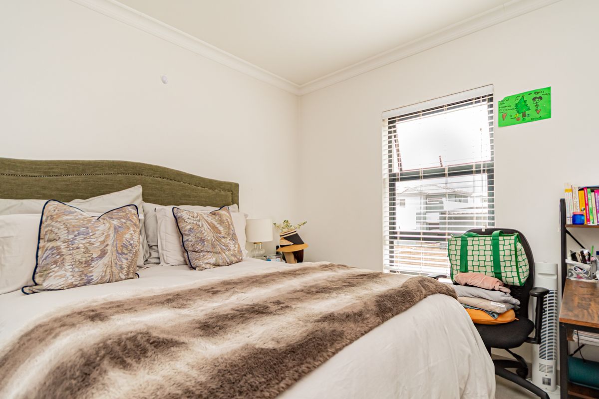 A well-lit bedroom featuring neutral walls, crown molding, and a window fitted with venetian blinds.