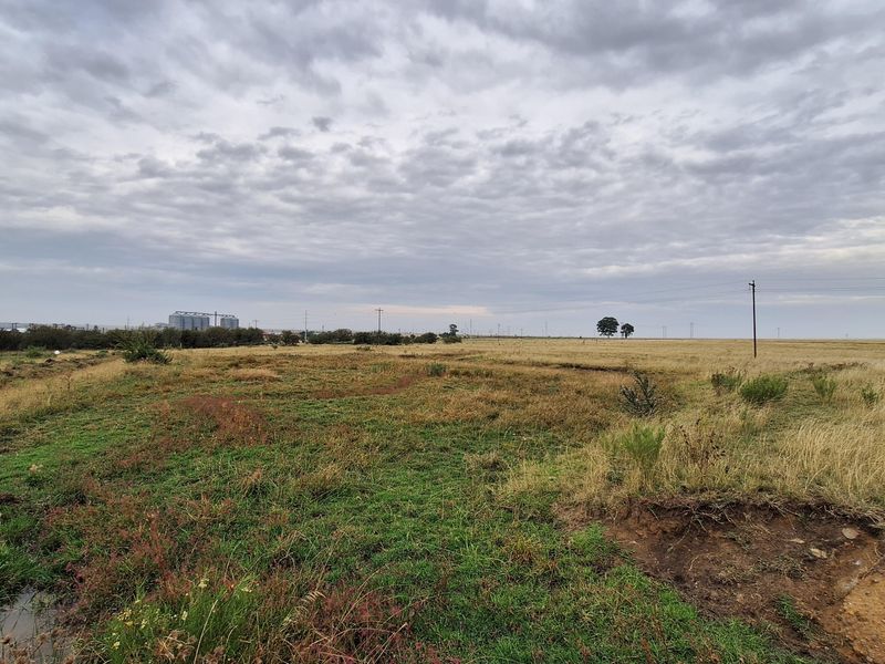 An expansive, undeveloped residential plot featuring natural grassland and open terrain under a cloudy sky.