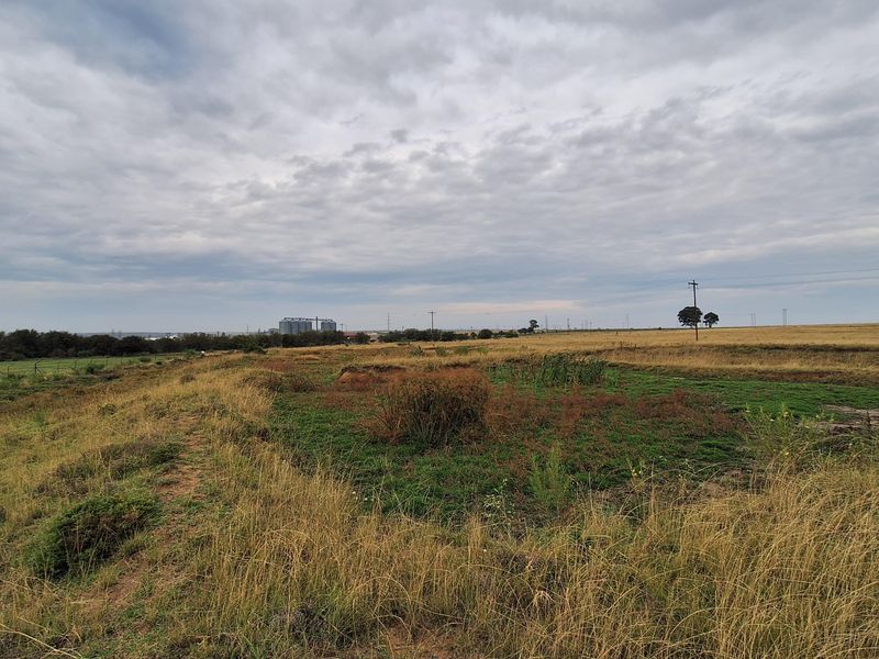 A wide-angle view of an expansive, undeveloped residential plot featuring natural grassland and distant utility infrastructure.