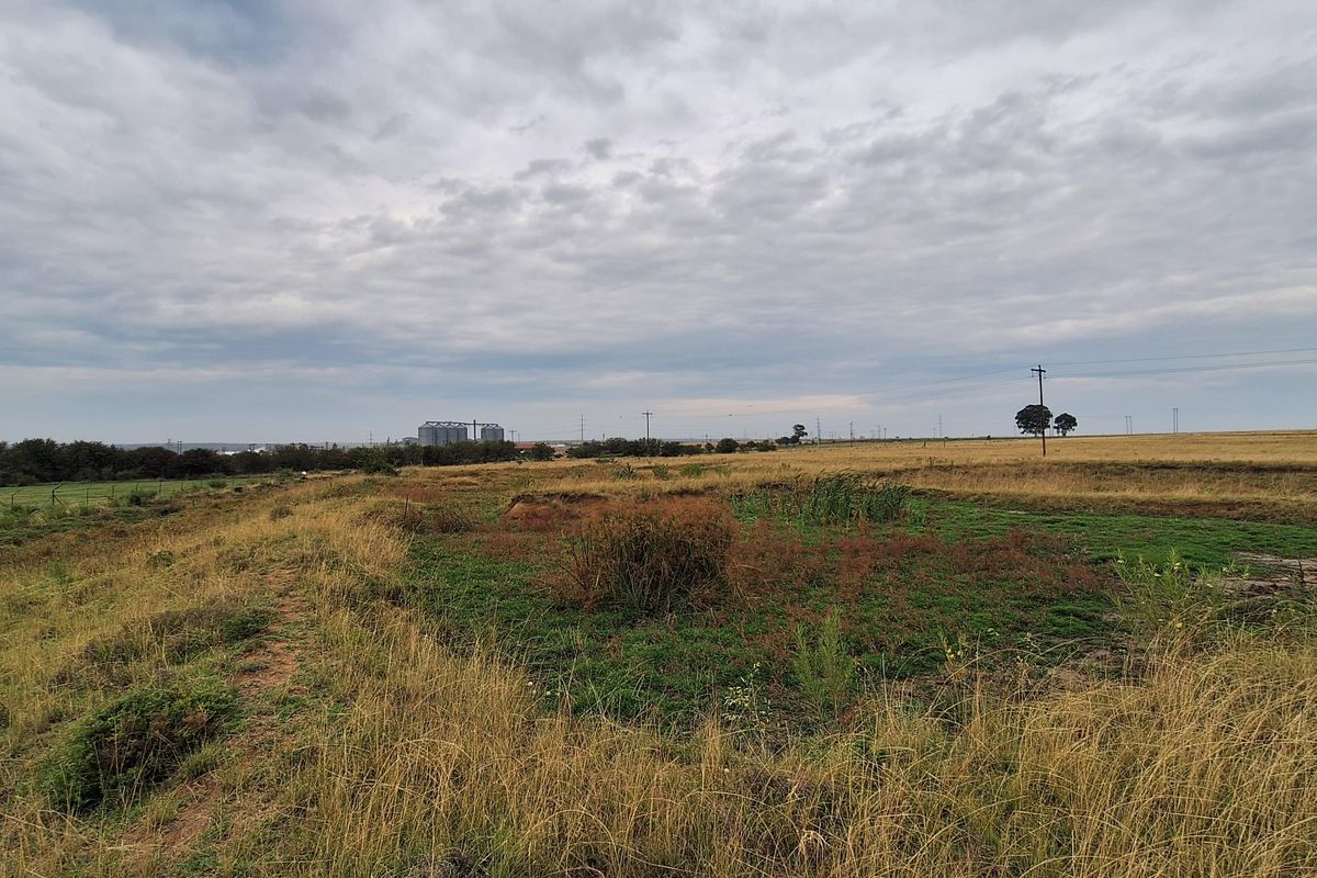 A wide-angle view of an expansive, undeveloped residential plot featuring natural grassland and distant utility infrastructure.