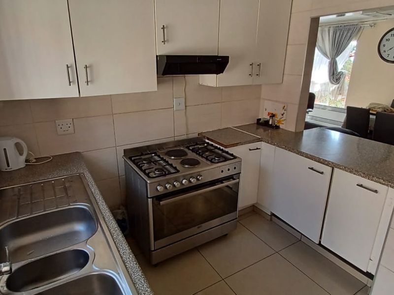 A functional kitchen featuring granite countertops, a gas stove with extractor fan, double bowl sink, and ample built-in cabinetry with tiled splashbacks.