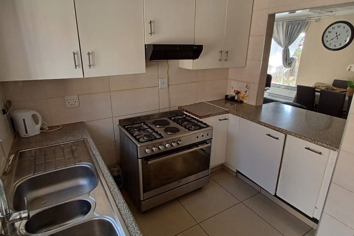A functional kitchen featuring granite countertops, a gas stove with extractor fan, double bowl sink, and ample built-in cabinetry with tiled splashbacks.