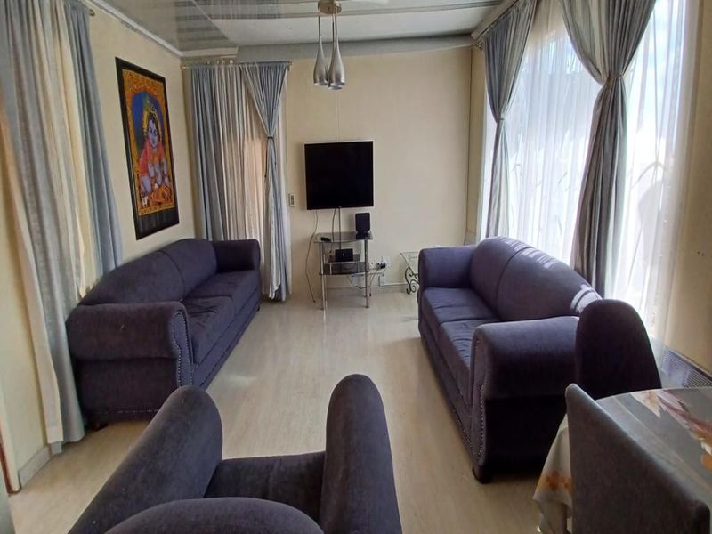 A living room featuring laminate flooring and ceiling panels, offering a functional space with natural light from large windows.