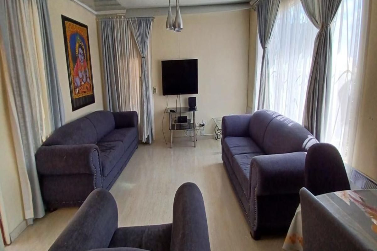 A living room featuring laminate flooring and ceiling panels, offering a functional space with natural light from large windows.