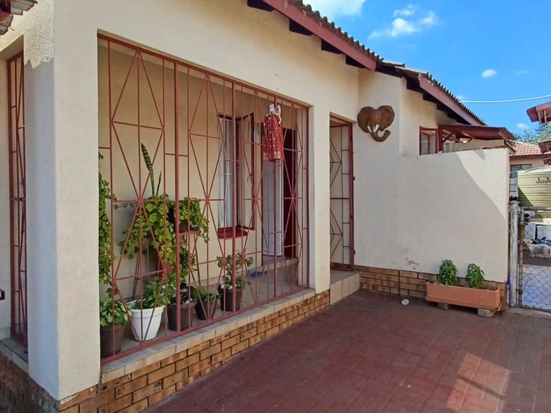 A covered patio area featuring security bars, brick paving, and access to the side yard with a water tank.