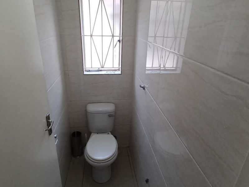 A compact, clean guest bathroom featuring neutral wall tiles, tiled flooring, and a window with security bars.