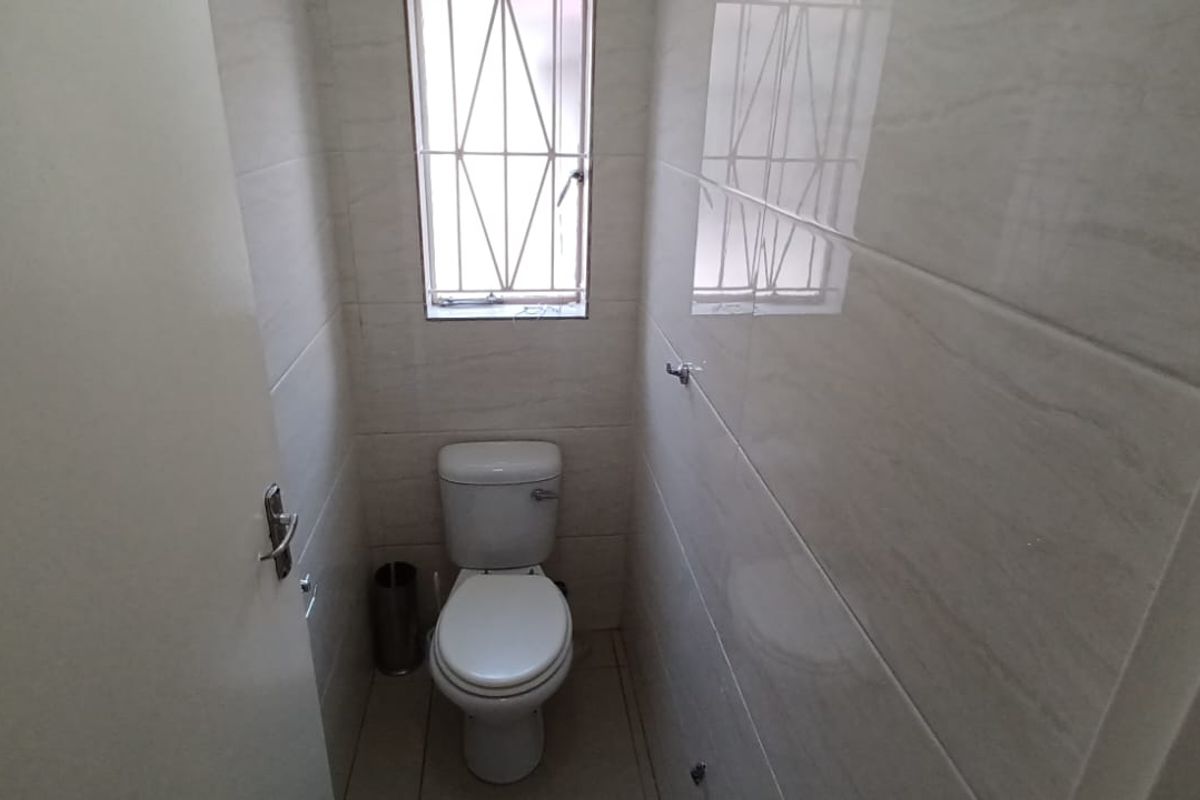 A compact, clean guest bathroom featuring neutral wall tiles, tiled flooring, and a window with security bars.