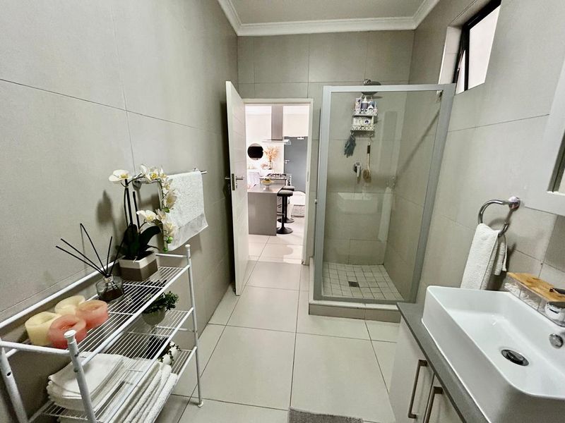 A modern bathroom featuring a glass-enclosed shower, a sleek vanity basin with storage, and neutral floor-to-ceiling wall tiles.