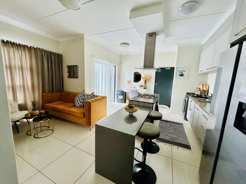 Modern open-plan living area featuring a sleek kitchen with a central island, gas hob, extractor fan, and tiled flooring throughout.