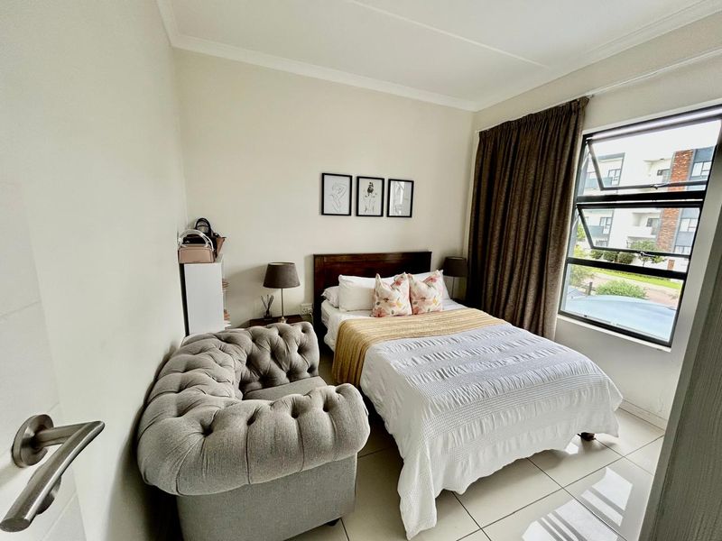 A well-lit bedroom featuring tiled flooring, a large window with curtain tracks, and neutral wall finishes.