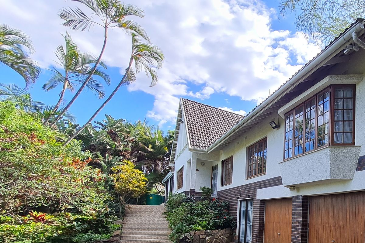 Rear view of a multi-level house featuring a tiled roof, brick and plaster facade, bay windows, double garage, and a landscaped garden with stone stairs.